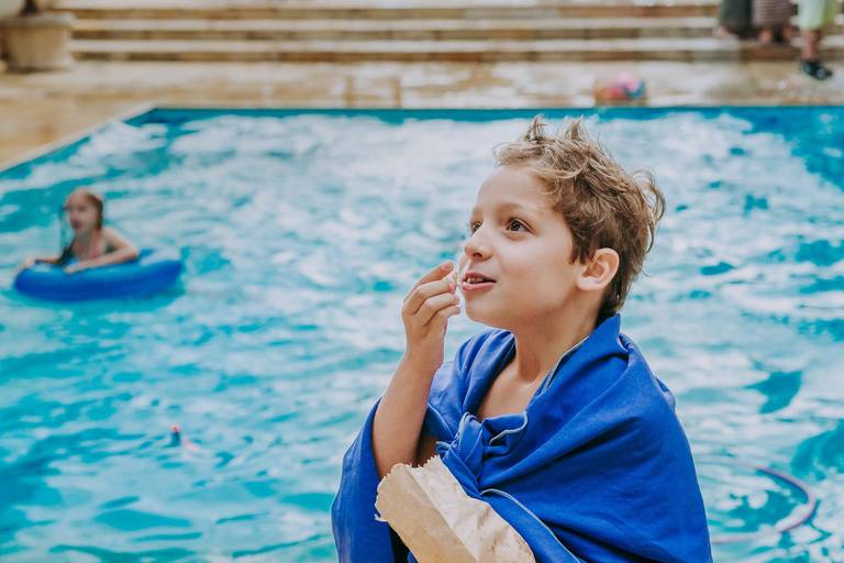 menino come pipoca em frente a piscina