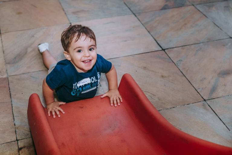 criança de dois anos sorri para a camera ao descer do escorrega
