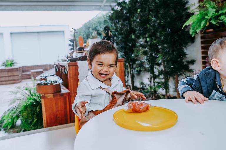 criança gargalha sentado a mesa olhando pra massinha de modelar