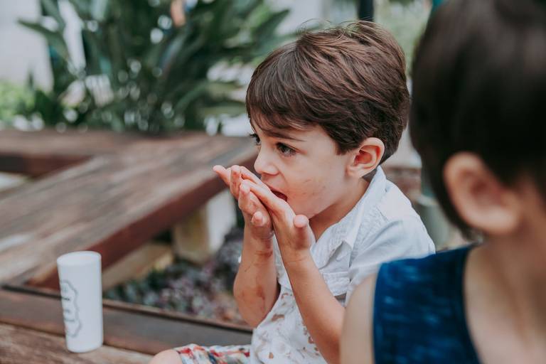 criança lambe avidamente sua mao lambuzada de sorbvete de chocolate