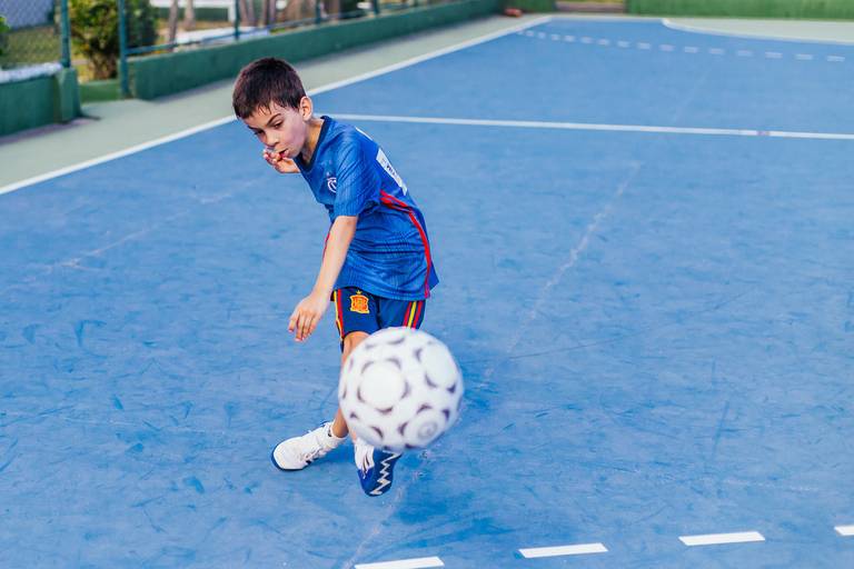 menino chuta a bola em direção à camera da fotografa que realizou um click certeiri