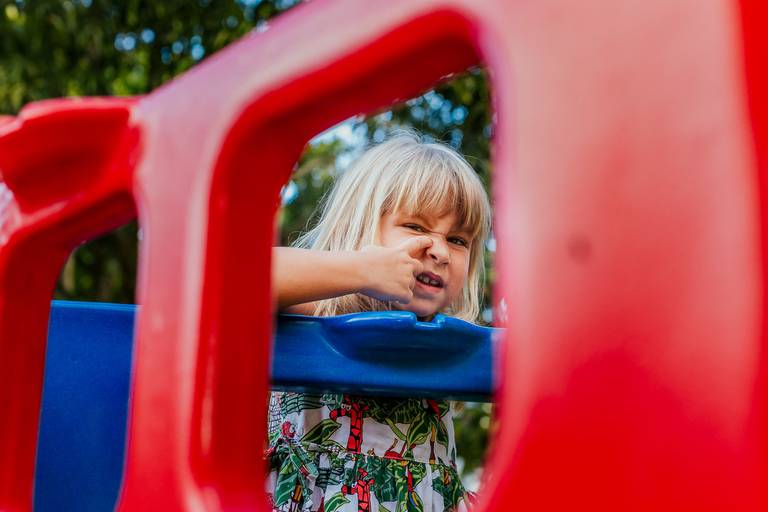 menina coçando naris enquanto brinca em brinquedo de parquinho de condominio