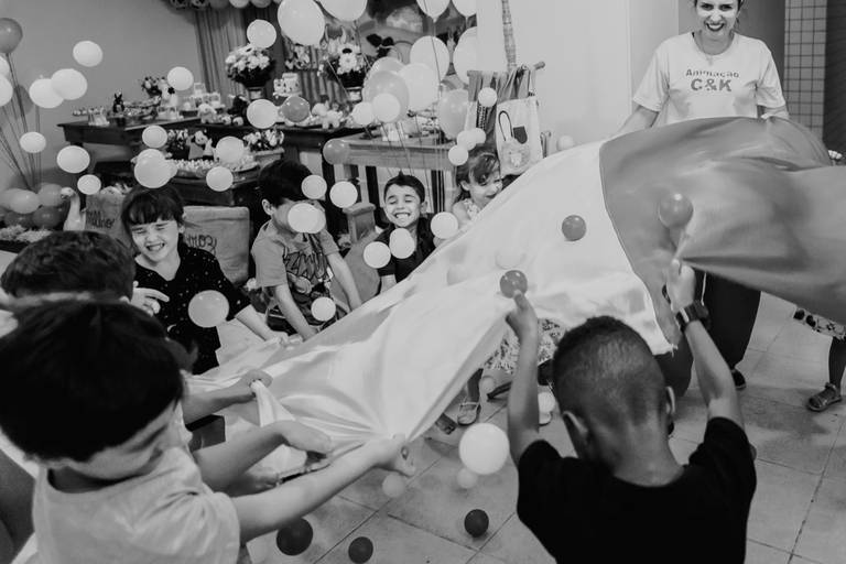 foto em preto e branco de crianças sacodem tecido e arremessam bolinhas de plastico para o alto