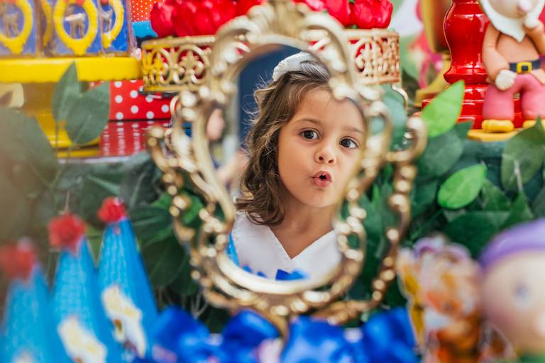 menina faz cara de surpresa ao se ver no espelho da branca de neve em seu aniversario