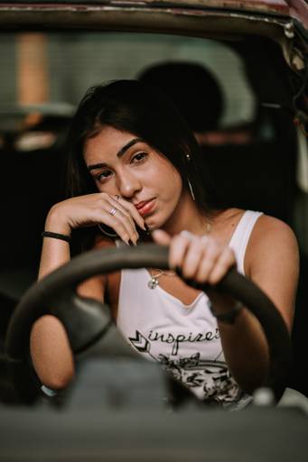 book de debutante fotografada dentro de carro no ferro velho na estrada do catonho no rj ela leva a mão direita ao rosto e a esquerda segura o volante