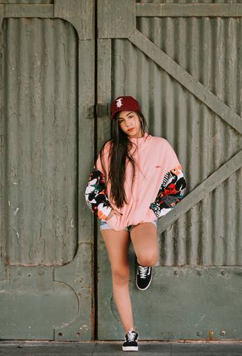 menina de short casaco e bone com uma perna dobrada e encostada no portão de um dos armazéns da praça mauá