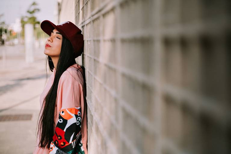 debutante de boné e casaco de olhos fechados encostada numa parede de quadradinhos