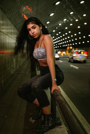 adolescente de 15 anos sentada em corrimão de túnel do rj atrás luzes das lanternas dos carros que passam