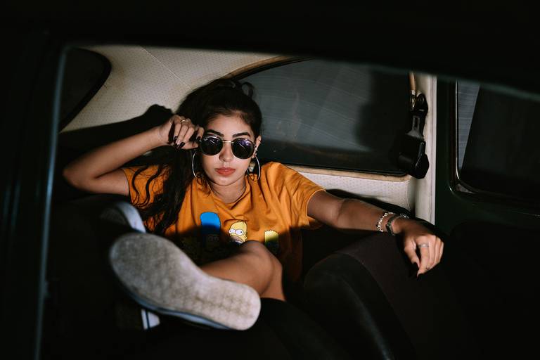 adolescente de óculos escuros sentada com as pernas para o alto no banco trazeiro de um fusca