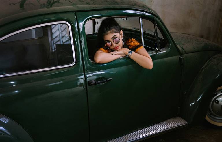 adolescente de 15 anos dentro de um fusca com os braços e o rosto apoiado na janela do carona e de óculos escuros