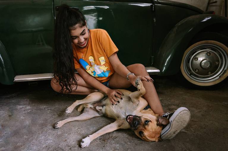 debutante com seu cachorro brincando no chão ao lado de um fusca antigo