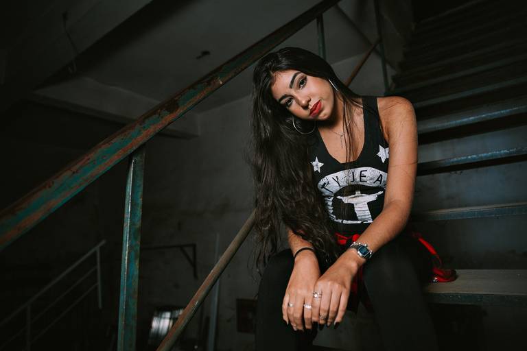 book debutante dentro de uma serralheria ela toda de preto sentada em uma escada