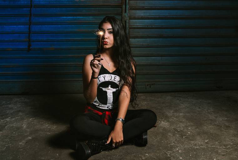 foto de debutante sentada no chao toda de preto dentro de uma oficina com uma vela faísca acesa em frente ao olho direito