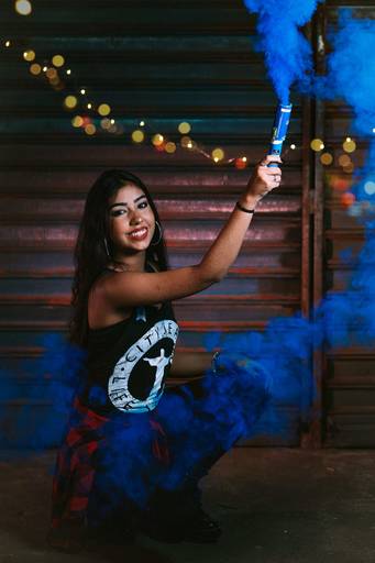 debutante acendendo fumaça azul dentro de uma oficina, atras dela luzes vermelha na porta da oficina