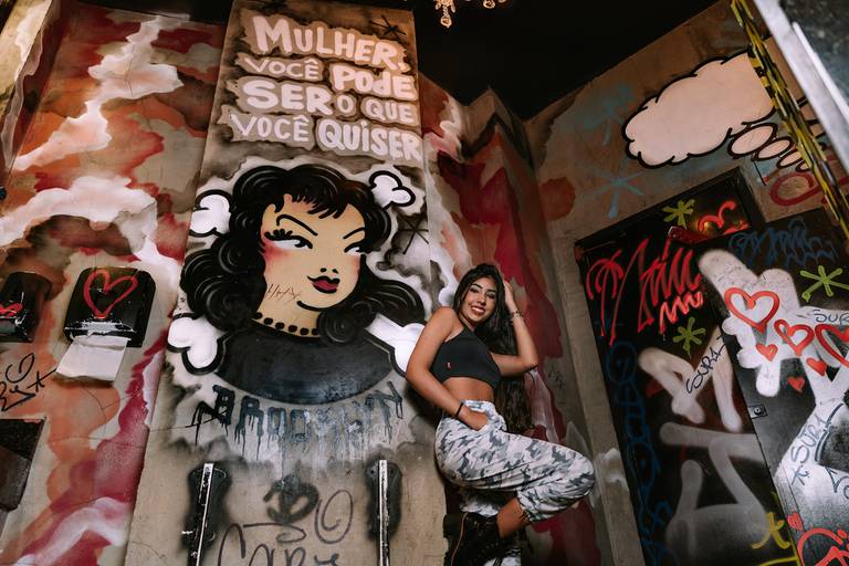 foto de baixo pegando todo o banheiro do bar do brooklin pegando as paredes pixadas e a debutante está encostada na parede ajeitando o cabelo