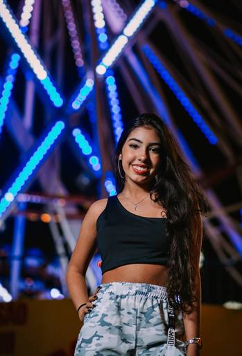 foto vertical de debutante de croped em frente a uma roda gigantecom luzes azuis a noite 