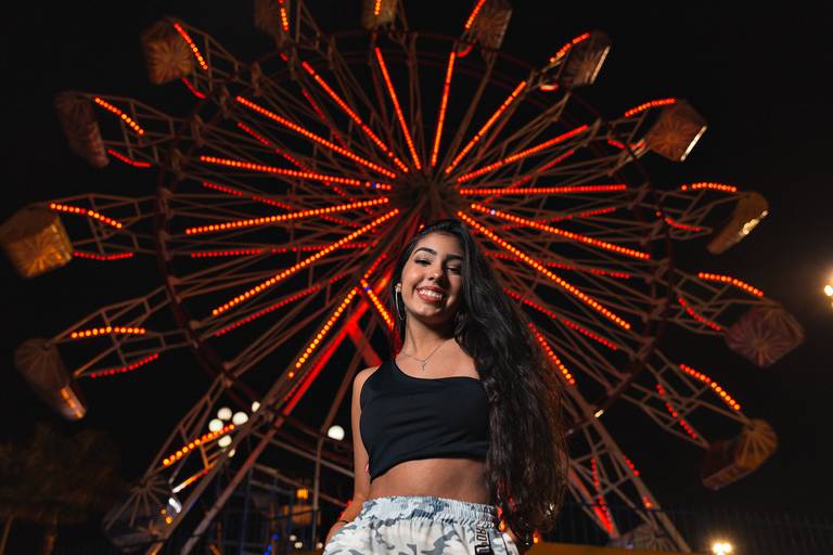roda gigante ao fundo com luzes vermelhas e debutante no centro em primeiro plano sorrindo para camera 