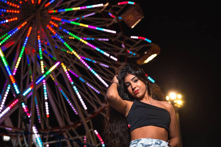 roda gigante ao fundo no canto esquerdo da imagem e menina debutante no canto  direito interior da foto com a mão no cabelo