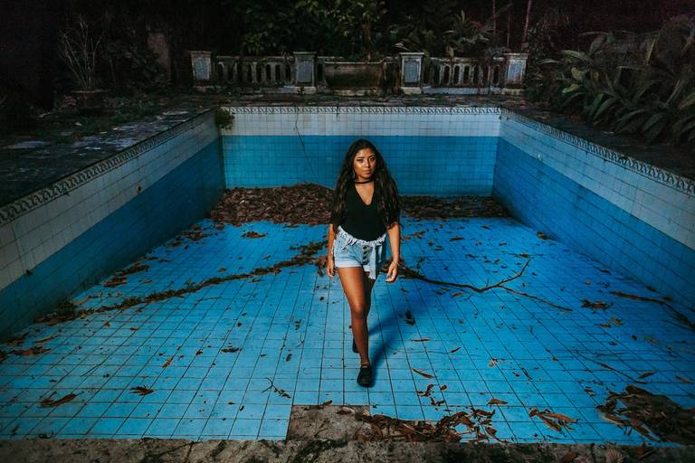 foto de menina debutante dentro de uma piscina grande vazia e abandonada cheia de folhas