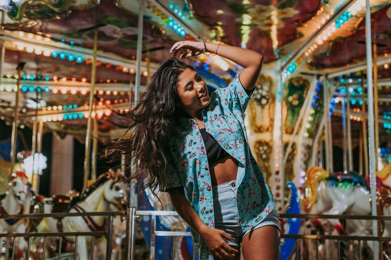 book de ensaio debutante em parque de diversoes carrossel ao fundo e menina de short e blusao mexendo nos cabelos