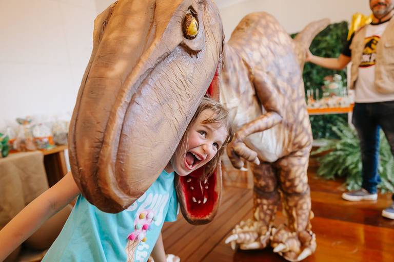 foto colorida com humor menina com a cabeça dentro da boca de personagem vivo dinossauro em festa infantil afetiva no recerio dos bandeirantes