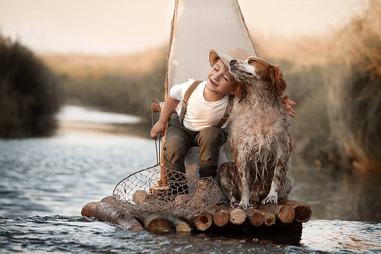 Niño en el río con mascota. Balsa de troncos con labrador en la sesión de fotos de Barby Massei