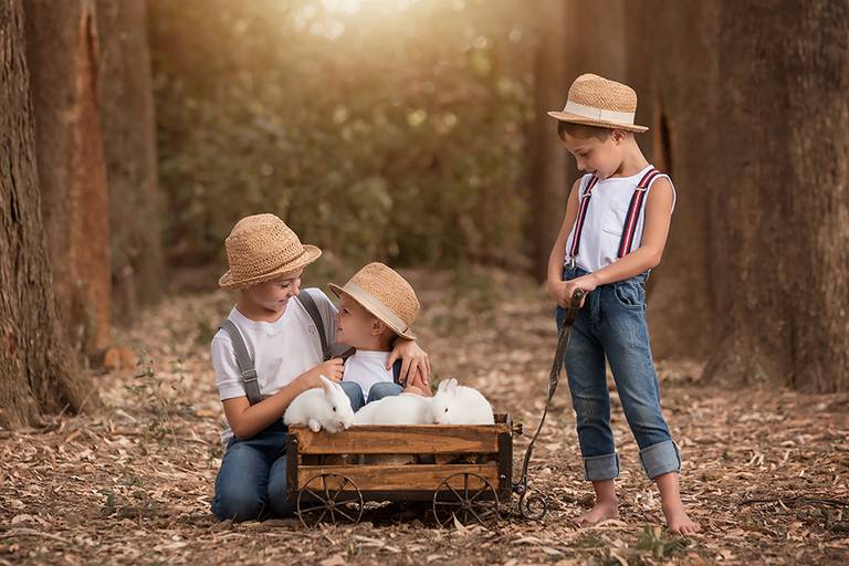 Hermanos jugando al atardecer en el campo. Carrito de madera para la sesión de fotos de Barby Massei. Book infantil.