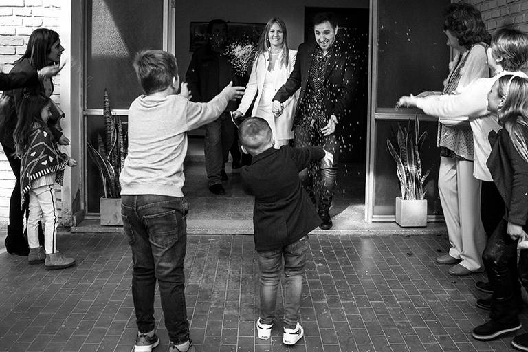 Salida de la ceremonia civil en San José de la Esquina, Santa Fe. Novios con arroz y niños arrojando. Foto blanco y negro. Barby Massei Fotografía.