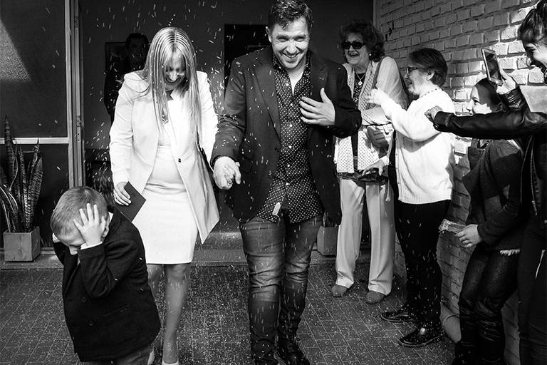 Niño con las manos en la cara en la salida de sus papis del registro civil, festejando junto a ellos. Alegría en las fotos. Civil en Santa Fe. Foto blanco y negro Barby Massei Fotógrafa. San José de la Esquina.