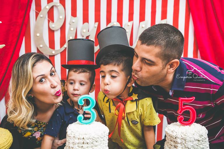 fotografia aniversário festa dupla aniversariantes vestidos de mágico soprando as velinhas ao lado dos pais na mesa do bolo com decoração tema circo