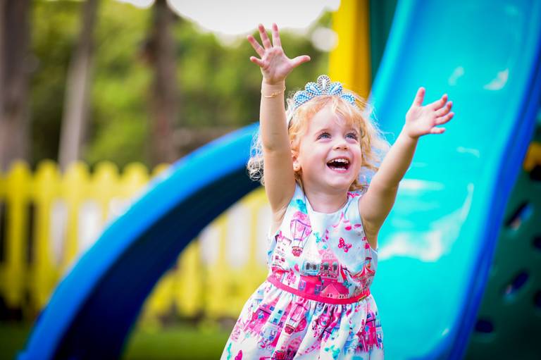 menina loira sorrindo com bracos levantados