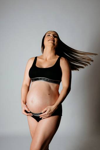 Ensaio gestante em estúdio, barriga está aparecendo, gestante está usando conjunto da Calvin Klein, faz movimento com o cabelo
