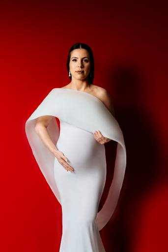 Ensaio gestante em estúdio, gestante utiliza um vestido branco de moulage, fundo da foto vermelho