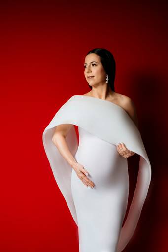 Ensaio gestante em estúdio, gestante utiliza um vestido branco de moulage, fundo da foto vermelho