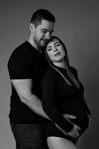 Ensaio gestante em estúdio, gestante é abraçada  na barriga pelo marido, foto em preto e branco, casal esta de olhos fechados