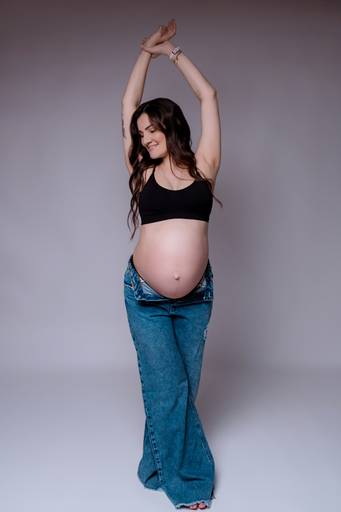 Ensaio gestante em estúdio, mulher scom sorriso leve com os braços para cima barriga a mostra 