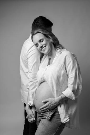 Ensaio gestante em estúdio, barriga a mostra, foto em preto e branco mulher apoiada no ombro do homem