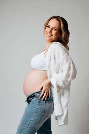 Ensaio gestante em estúdio, barriga a mostra, gestante com mãos na cintura sorrindo