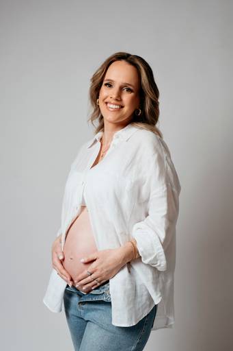 Ensaio gestante em estúdio, barriga a mostra, gestante com as mãos na barriga olha para camera e sorri