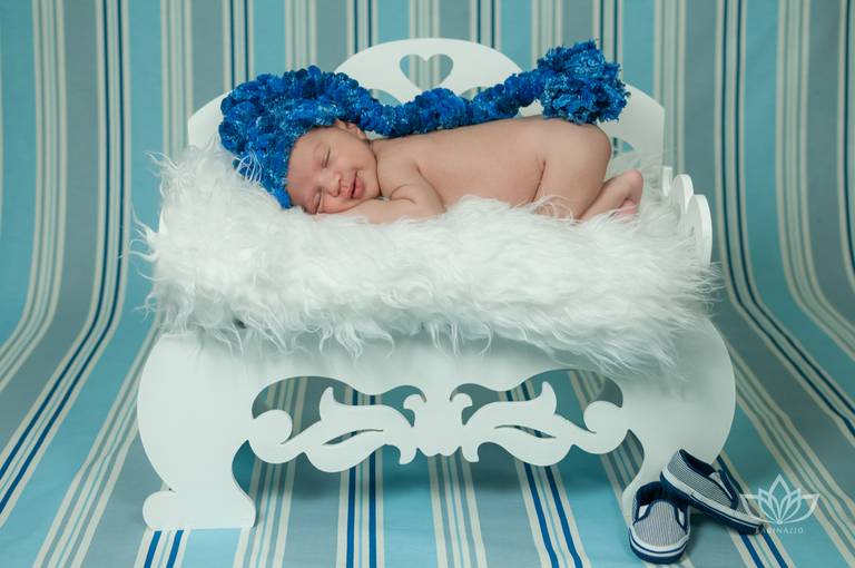 Ensaio Newborn tons de azul com bebê recém nascido deitado no banquinho com touca newborn azul.