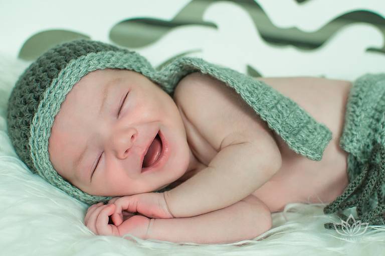 Ensaio Newborn com bebê recém nascido sorrindo deitado no banquinho com touca aviador newborn.