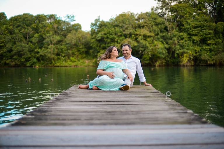 Ensaio de gestante fotografado pelo melhor fotógrafo de ensaios de campo largo e Curitiba. Gestante e marido sentados na ponte lago verde 