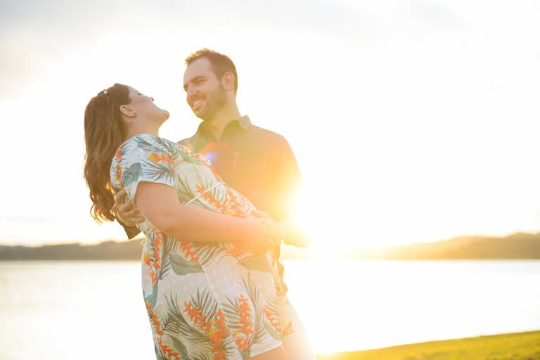Ensaio de gestante fotografado pelo melhor fotógrafo de ensaios de campo largo e Curitiba. Casal sorrindo em frente ao lago, por do sol