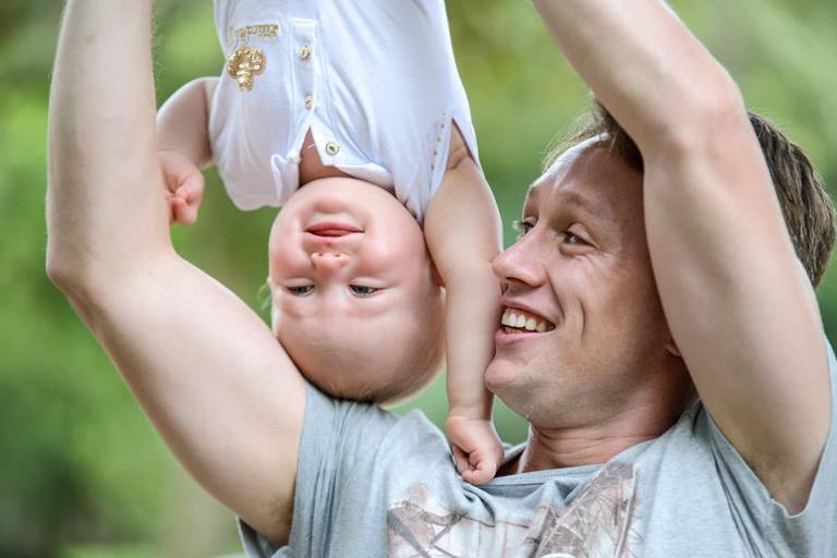 Família feliz, pai, mãe e filha fotografados pelo melhor fotógrafo de Curitiba e Campo Largo, Michel Druziki. Pai segurando bebê de cabeça pra baixo