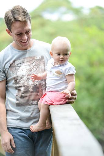 Família feliz, pai, mãe e filha fotografados pelo melhor fotógrafo de Curitiba e Campo Largo, Michel Druziki. Pai cuidando da filha sentada na varanda