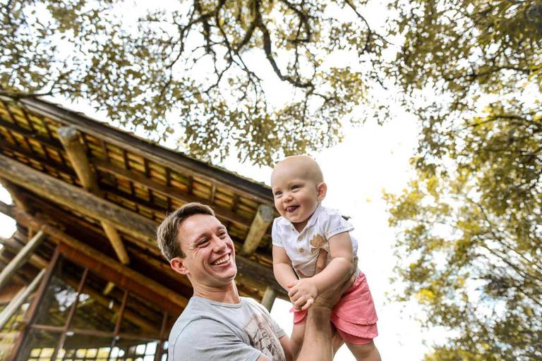Família feliz, pai, mãe e filha fotografados pelo melhor fotógrafo de Curitiba e Campo Largo, Michel Druziki. Pai brincando de aviãozinho com a filha