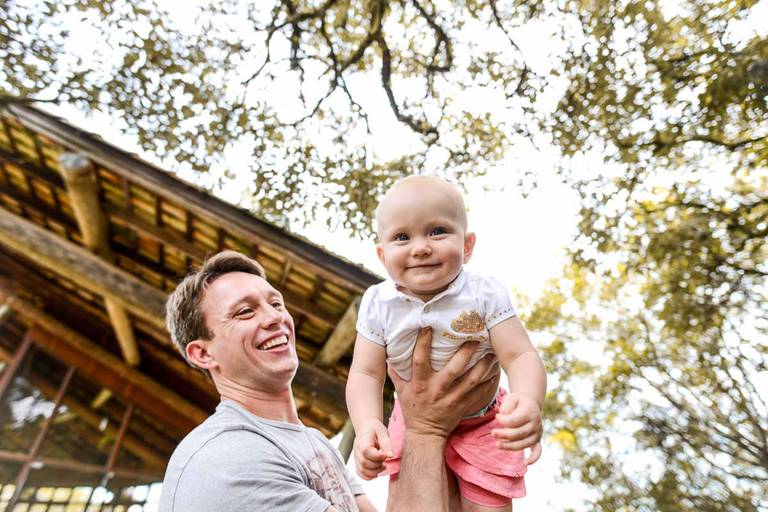 Família feliz, pai, mãe e filha fotografados pelo melhor fotógrafo de Curitiba e Campo Largo, Michel Druziki. Pai brincando de aviãozinho com a filha