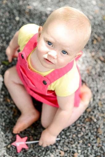 Família feliz, pai, mãe e filha fotografados pelo melhor fotógrafo de Curitiba e Campo Largo, Michel Druziki. Bebê com jardineira sentada no chão olhando pra cima