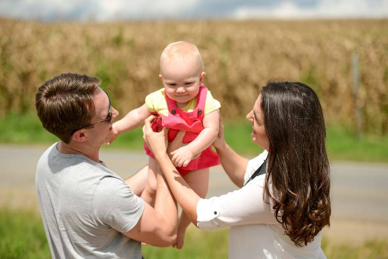 Família feliz, pai, mãe e filha fotografados pelo melhor fotógrafo de Curitiba e Campo Largo, Michel Druziki. Pais erguendo a filha no campo