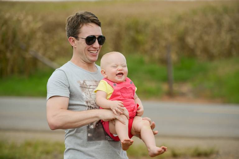 Família feliz, pai, mãe e filha fotografados pelo melhor fotógrafo de Curitiba e Campo Largo, Michel Druziki. Bebê dando risada no colo do pai